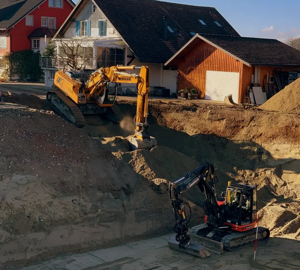Zwei Bagger arbeiten in einer Baugrube vor Wohnhäusern