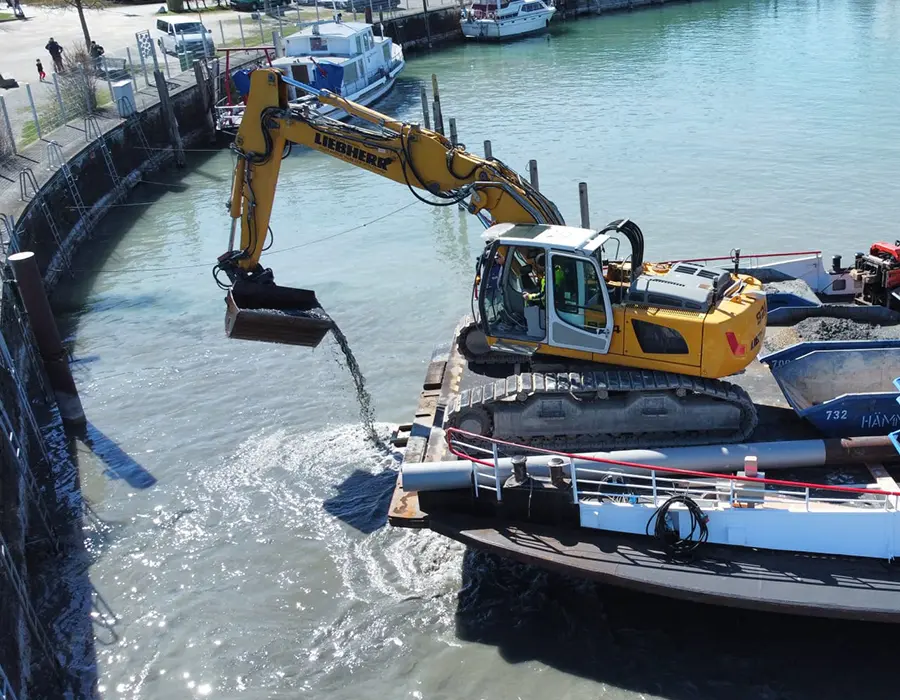 Bagger entnimmt Material aus dem Wasser von einem Ponton aus